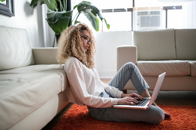 Blog image Woman working at home from her laptop, sitting on the ground on top of a bright red carpet